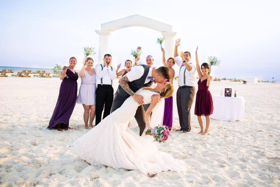 Wedding party posing in front of beach wedding arch